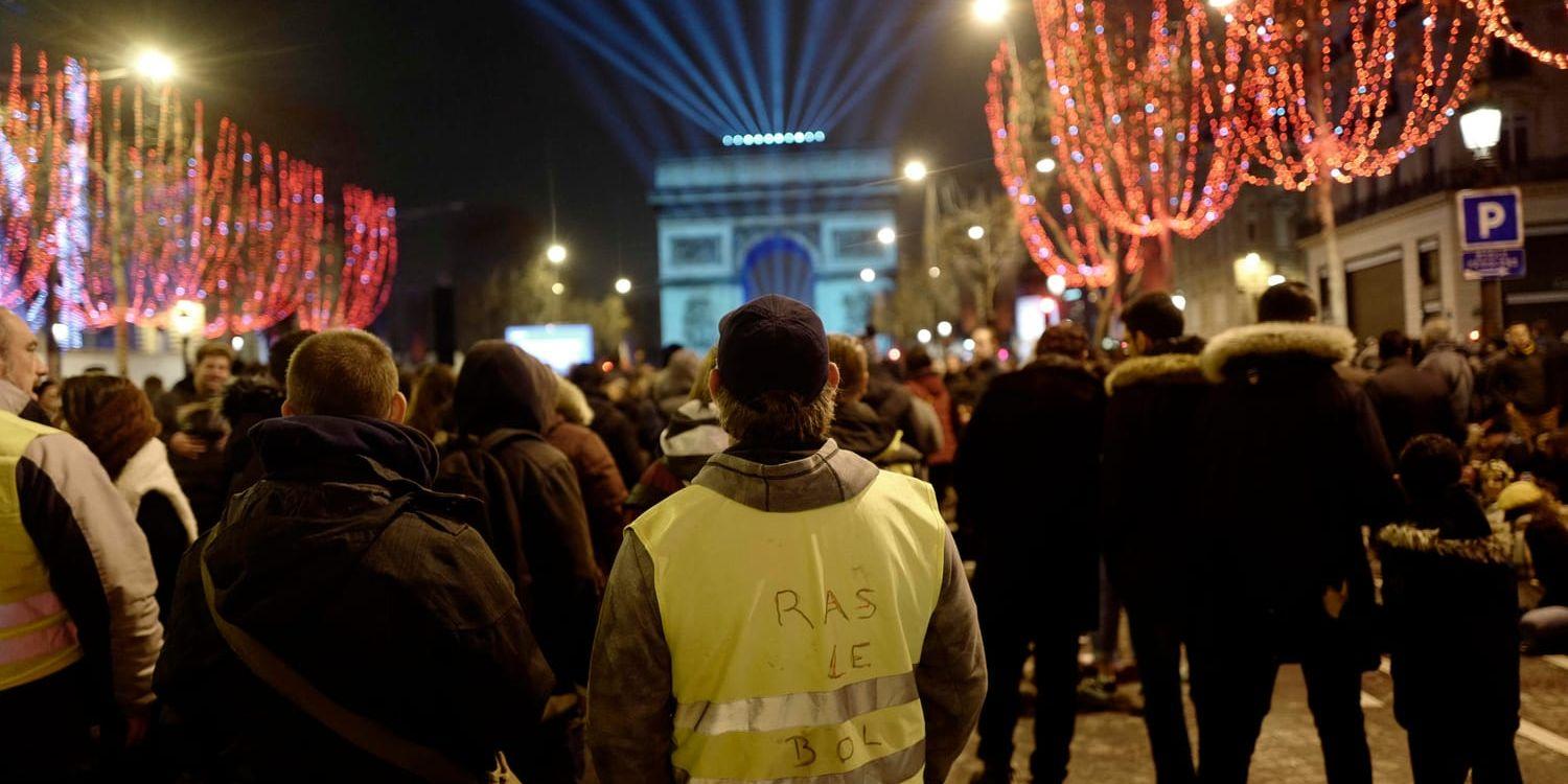 Demonstranter från Gula västarna tittar på ljusspelet över Triumfbågen i centrala Paris på nyårsafton.