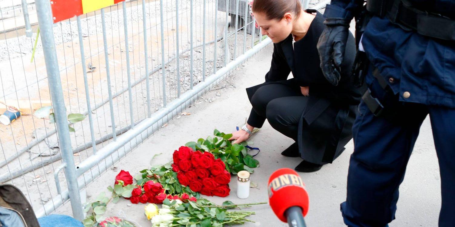 Kronprinsessan Victoria lägger blommor vid attentatsplatsen. Det finns tillfällen då journalister och deras mikrofoner får vänta.