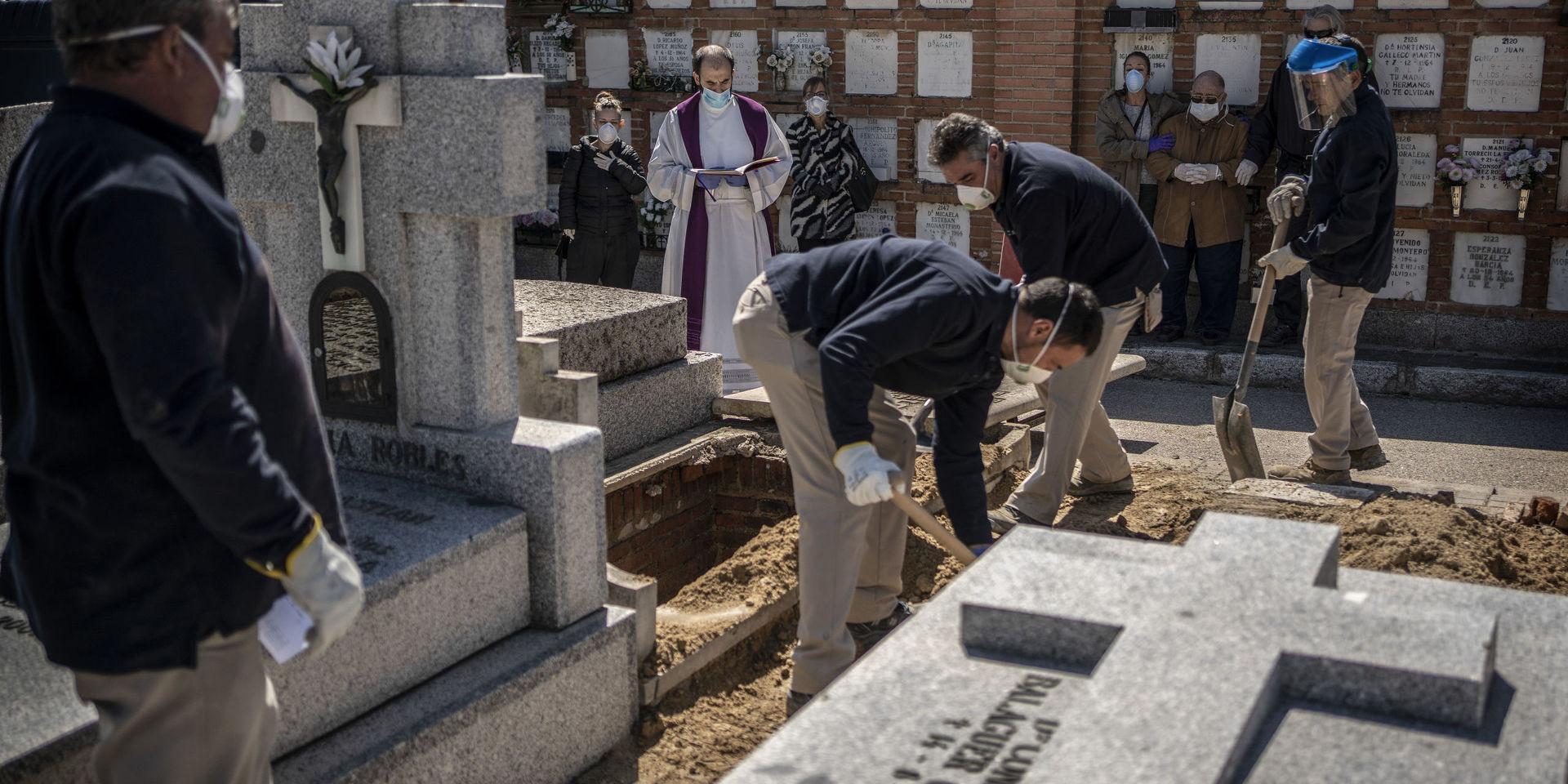En präst och anhöriga ber en bön i samband med att en person som avlidit i covid-19 begravs på en kyrkogård i Madrid.