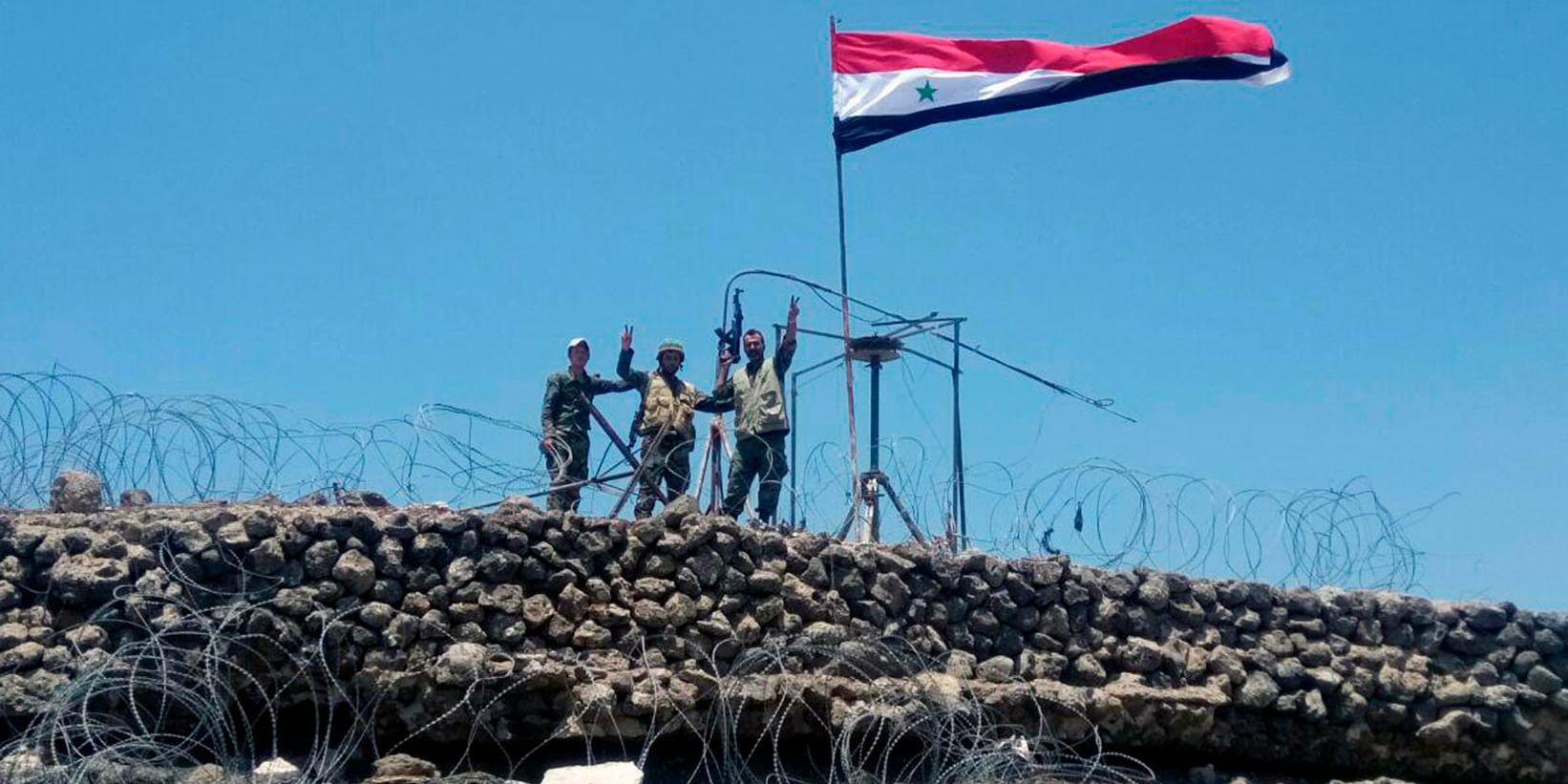 Soldater gör segertecknet intill den syriska flaggan på en höjd i Daraaprovinsen i södra Syrien. Arkivbild.