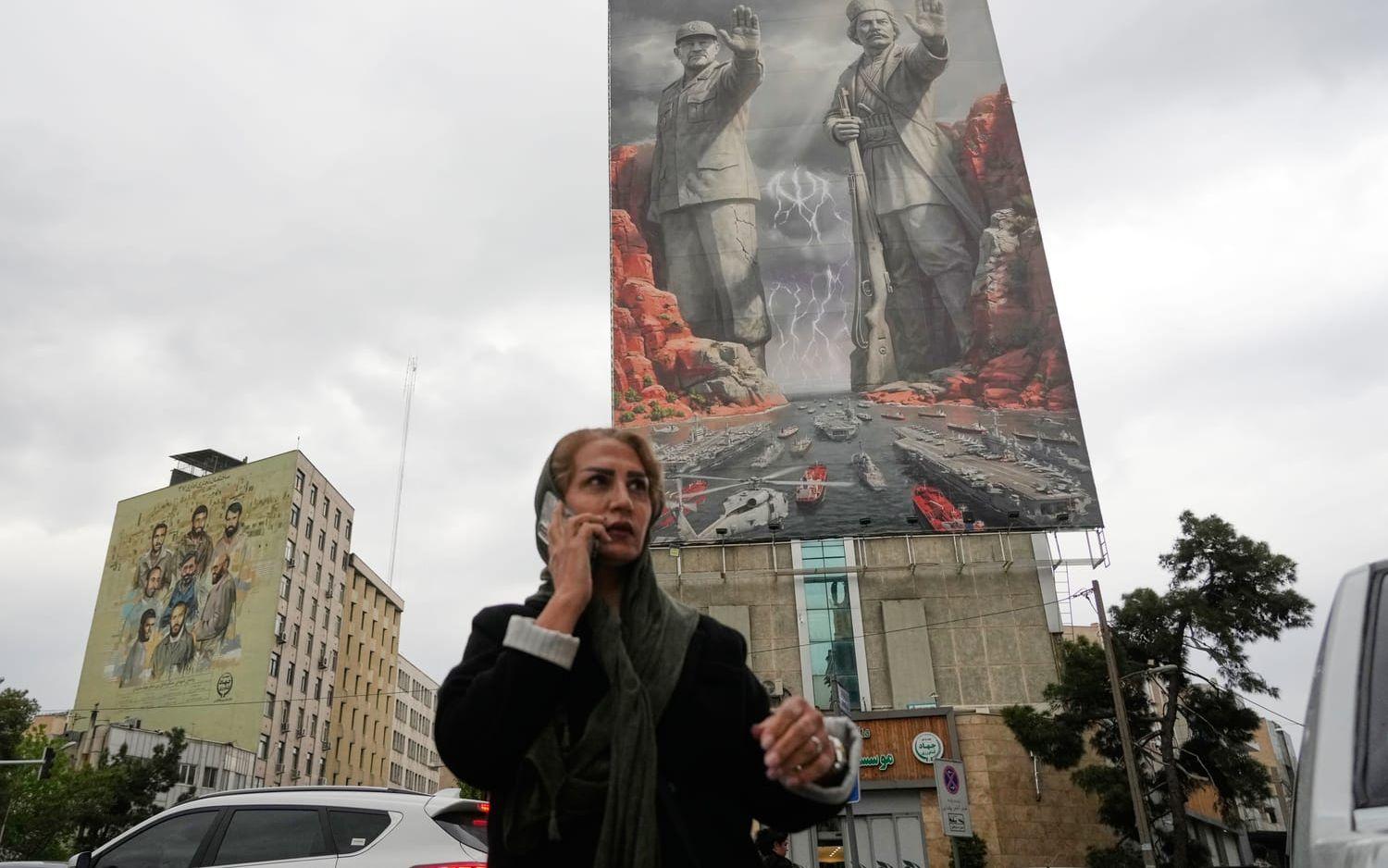 En kvinna talar i telefon på gatan i Teheran i måndags. I bakgrunden sitter ett stort propagandabanér där en av Revolutionsgardets nyligen dödade ledare och en iransk nationalhjälte från tidiga 1900-talet poserar i en Sagan om ringen-inspirerad miljö.
