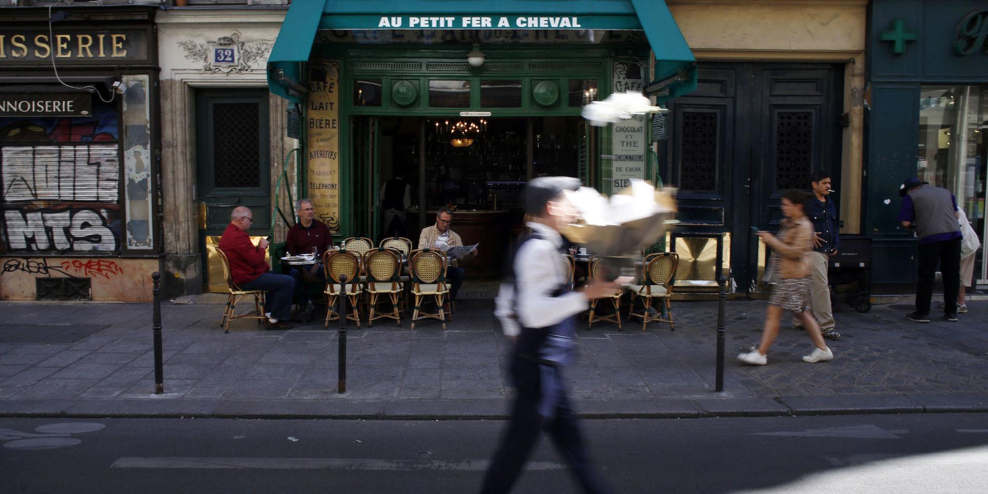 En man passerar med en bukett blommor framför ett café i stadsdelen Marais i Paris. Bild från september 2019.