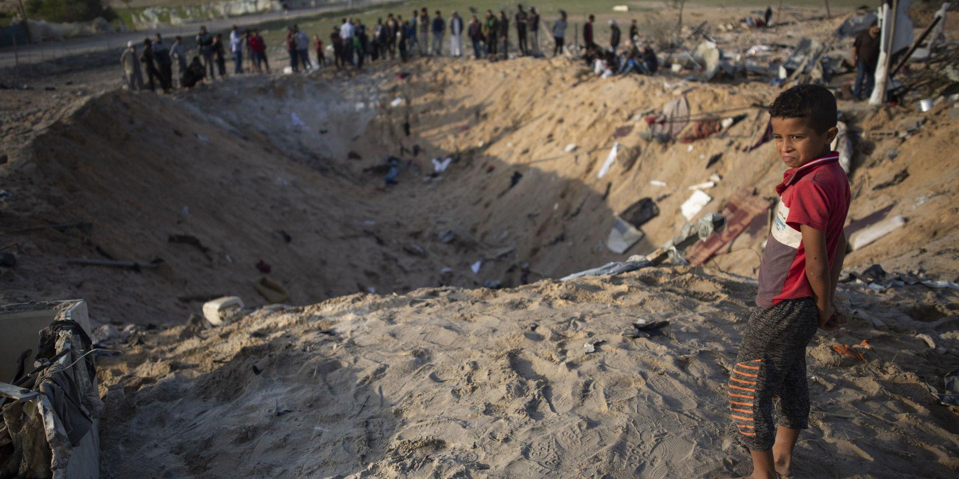 Människor som på torsdagen samlats kring kratern på Gazaremsan där Rasmi Abu Malhous bostad fanns innan den utsattes för en israelisk attack. 