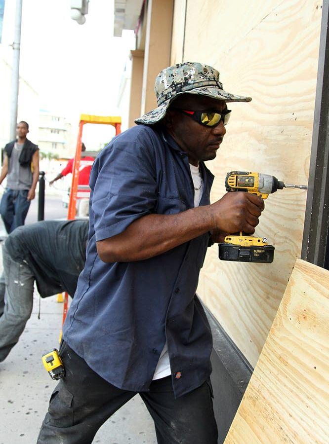 Yorick Bain skruvar fast plywood över fönstren på en Dunkin Donuts-affär i Nassau, Bahamas. Efterfrågan på material som plywood och sand har medfört att sådana produkter är slut i affärerna. Foto: Tim Aylen