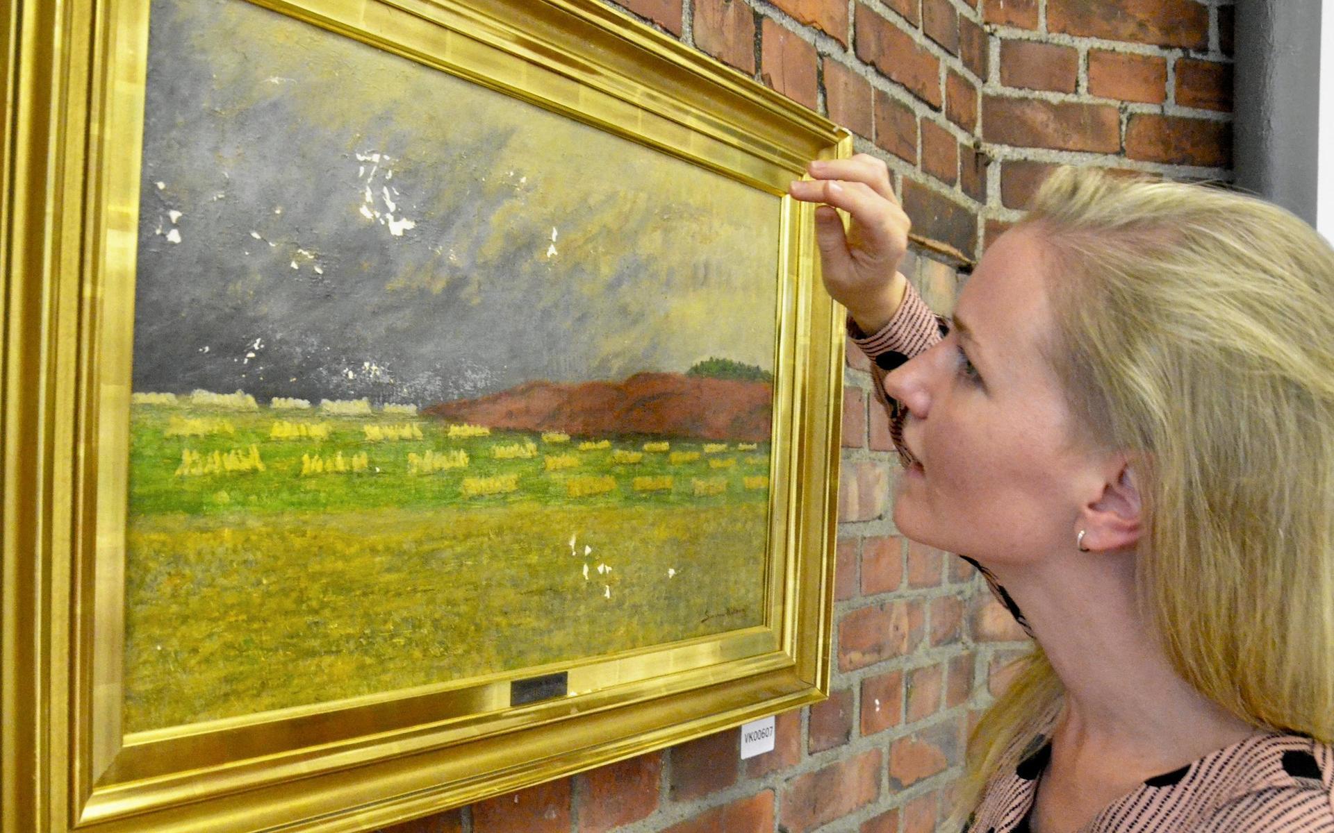 Kommunens konstkoordinator Cecilia Jonasson kollar skadorna på Severin Nilsons över 100 år gamla målning.