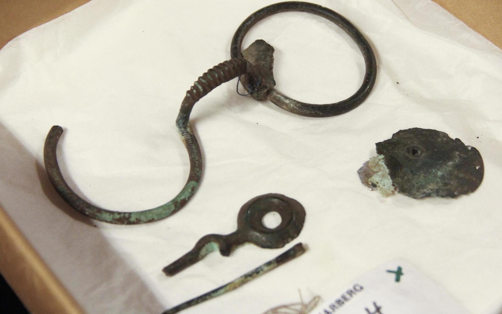 Ett glasögonformat spänne hittades ungefär där Nackhälleskölden upptäcktes. Längst ner syns en nål använda till hår eller kläder. Till höger: en avsatsyxa.