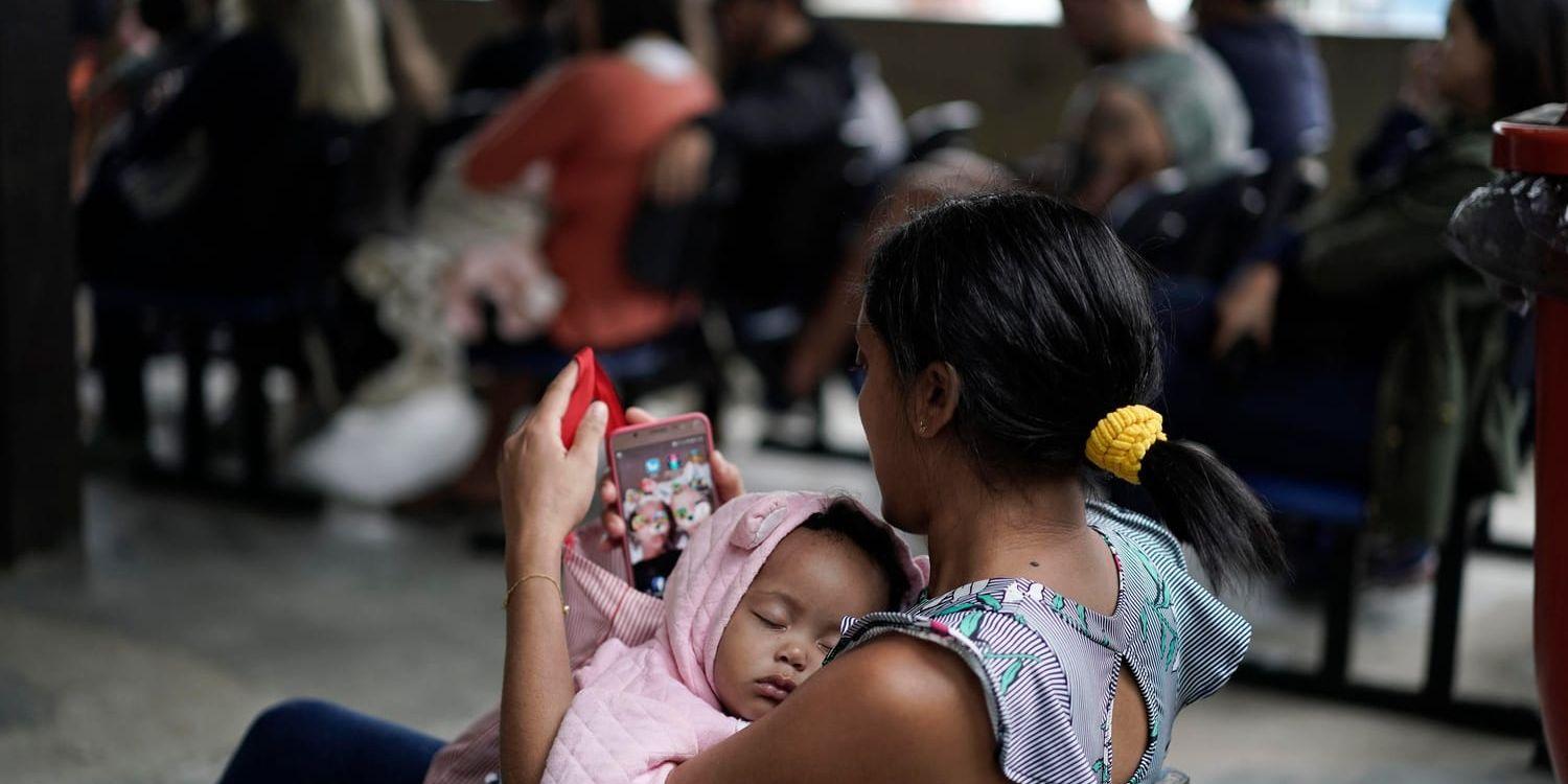 En mor vaggar sitt barn i väntan på vaccinering i brasilianska Rio de Janeiro i augusti i år.