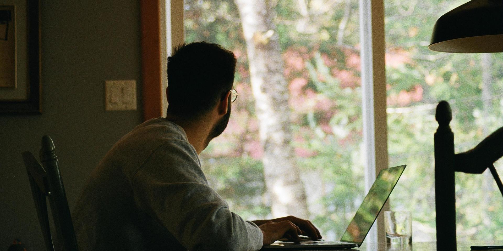En personer sitter vid dator och tittar ut genom ett fönster. 
