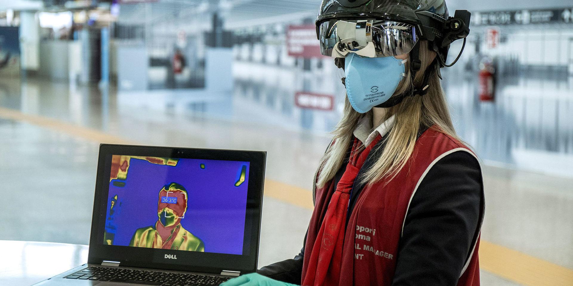 En medarbetare vid Romflygplatsen Leonardo da Vinci använder sig av en så kallad smarthjälm för att mäta kroppstemperaturen hos passagerare.