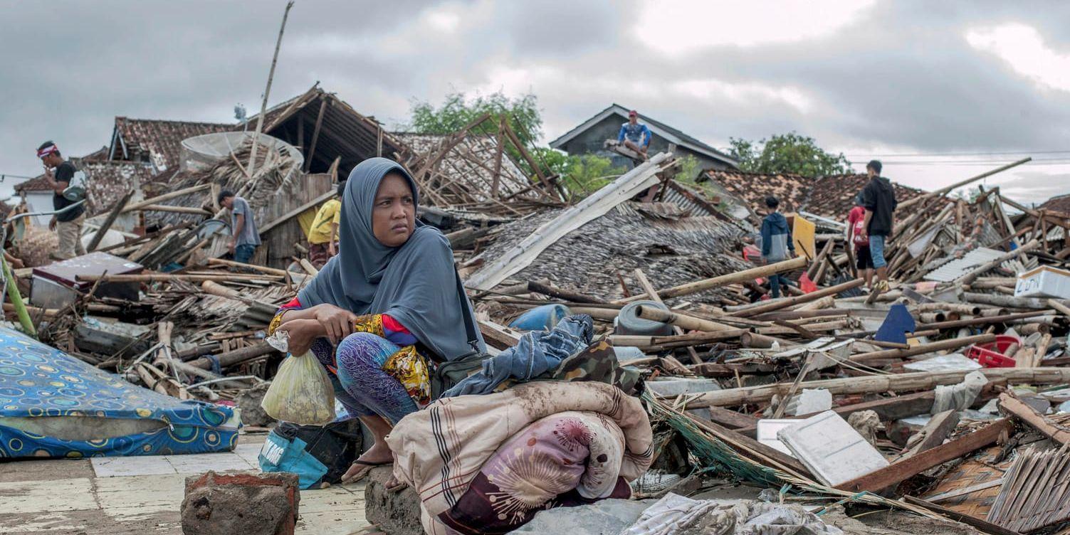 En tsunamiöverlevare vilar efter att ha försökt hitta ägodelar bland rasmassorna vi hennes förstörda hus i samhället Sumur.