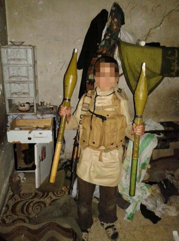 En av sönerna, som här ser ut att vara i tioårsåldern, poserar med granater till ett raketgevär. Han blev senare dödad när han var barnsoldat för IS.